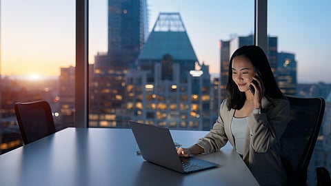Businesswoman works on laptop in modern office with city skyline at sunset