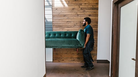 Mover carrying a green sofa through a hallway during a relocation
