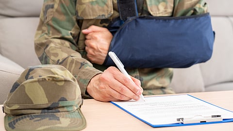 Injured veteran in camouflage uniform signing disability claim paperwork