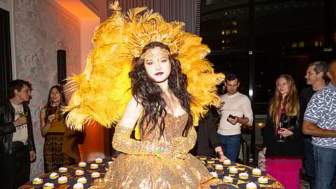 Performer in gold feathered costume presents desserts