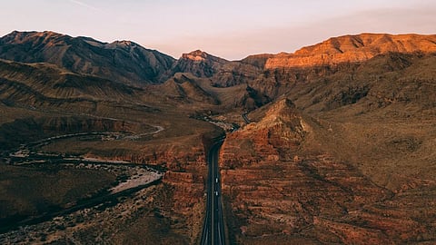 A winding road cuts through sunlit Arizona mountains at sunset