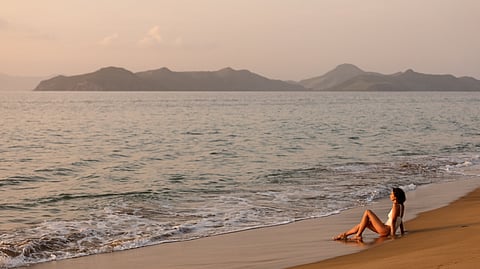 Woman relaxing on Paradise Beach at sunset with Nevis Peak in the distance