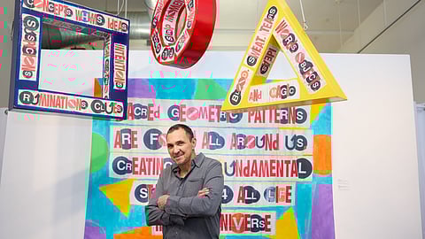 Al Diaz posing with text-based artworks at his “An Empire Fallen” exhibition