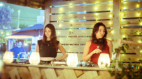 Two DJs performing at The Triangle’s outdoor bar with warm lights behind them