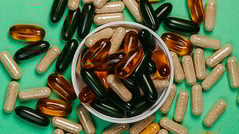Assorted capsules and softgels scattered on a green surface around a small bowl