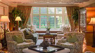 Elegant living room interior with patterned chairs, warm lighting, and large windows