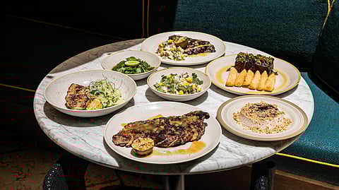 Table set with multiple wood-fired dishes, including grilled steaks and sides at Mayfair Grill