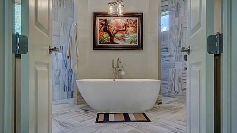 Freestanding bathtub centered in a marble-tiled luxury bathroom with soft lighting and art accent