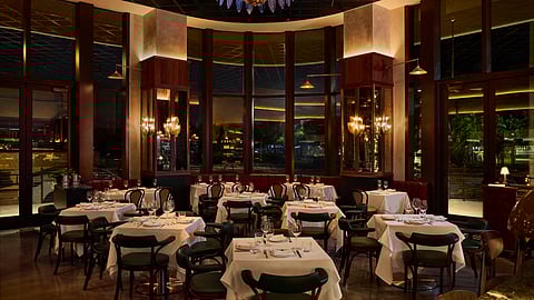 The main dining room at Ezio’s with white tablecloths, warm lighting, and a statement chandelier