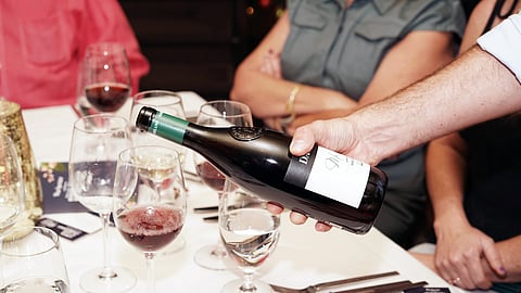 A hand pours red wine into glasses at a seated tasting table during a food and wine event