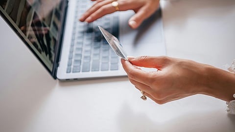 A person holding a credit card while using a laptop, representing digital transactions