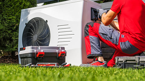 HVAC technician in red uniform performing maintenance on a high-efficiency outdoor heat-pump system