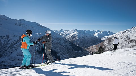 Ski guide assisting a guest on a snowy ridge with sweeping Swiss alpine mountains in view