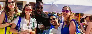 Group of friends smiling with drinks at SOBEWFF under a sunny beachside umbrella