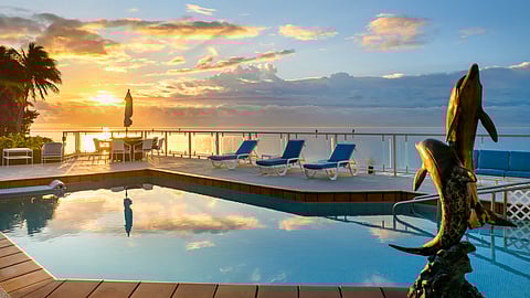 Sunrise over a waterfront pool deck with lounge chairs, glass railing, and Biscayne Bay beyond