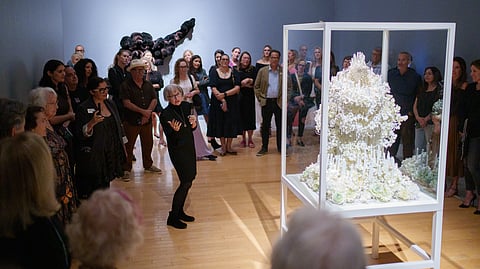 Petah Coyne speaking beside her sculpture “Zelda” in a glass vitrine at Lowe Art Museum