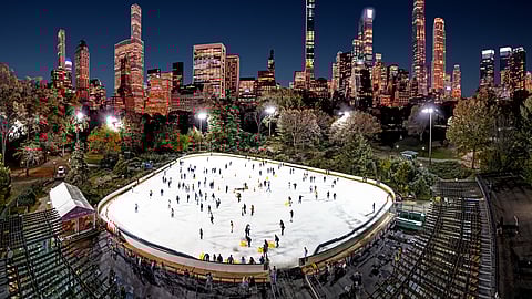 Wollman Rink at night with skaters and illuminated Manhattan skyline