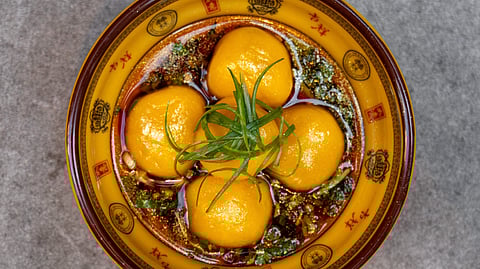 Overhead view of golden potato dumplings in chili-herb oil, topped with scallions
