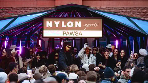 Crowd gathers under a NYLON Après PAWSA sign as DJ performs at a snowy outdoor event
