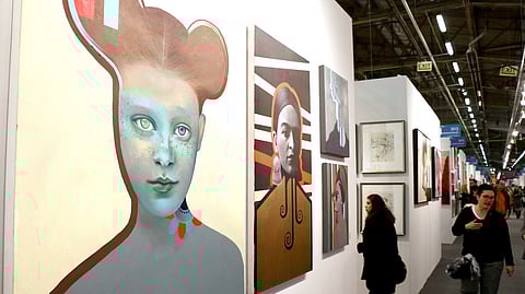 Visitors walk past large-scale contemporary portraits at Artexpo New York art fair