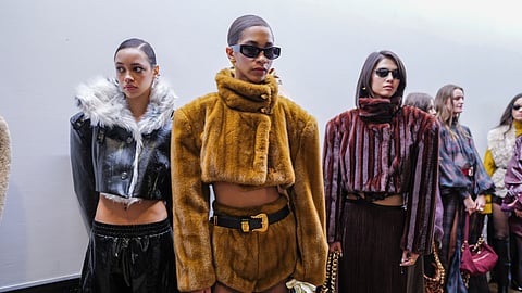 Models in fur, leather, and plaid looks stand backstage before the runway show