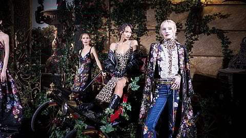 Models pose in floral gowns, leopard print, and embroidered denim beside a vintage car