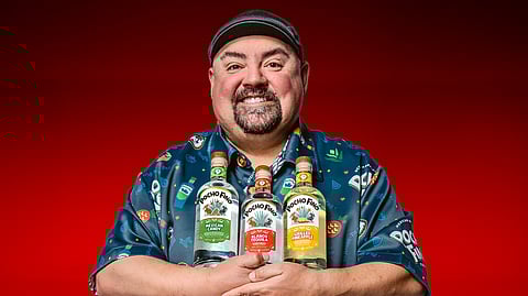 Gabriel “Fluffy” Iglesias posing with Pocho Fino tequila bottles against a red background