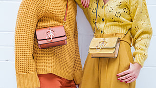 Two women wearing textured yellow knits and crossbody handbags in warm neutral tones