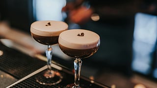 Close-up of two espresso martinis with creamy foam and coffee beans on a bar counter in NYC