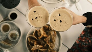 Overhead view of two espresso martinis with foam and coffee beans above a dessert table
