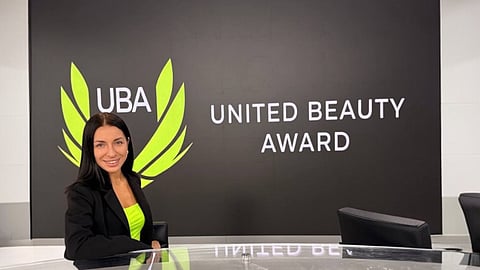 Woman posing at United Beauty Award UBA backdrop promoting global beauty industry event