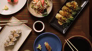 Assorted sushi and small plates on a wooden table with chopsticks and dipping sauces