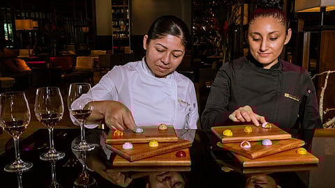Chefs preparing chocolate bonbons with wine glasses on a table in a dimly lit restaurant