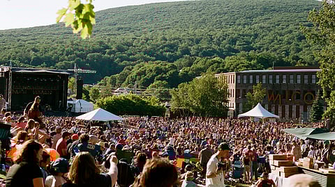 Outdoor crowd at MASS MoCA music festival with stage and mountains