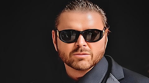 Ciro Dapagio in a black suit with red tie and sunglasses in studio portrait