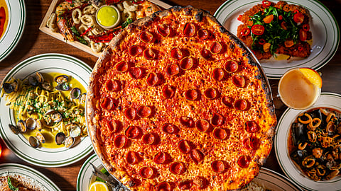 A large pepperoni pizza with pasta, seafood, and Italian plates on table