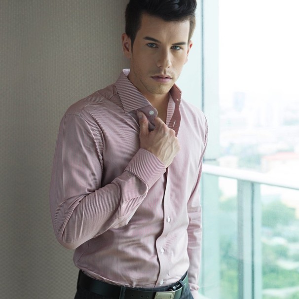 Man adjusting a tailored dress shirt near a window, showcasing fit and fabric detail