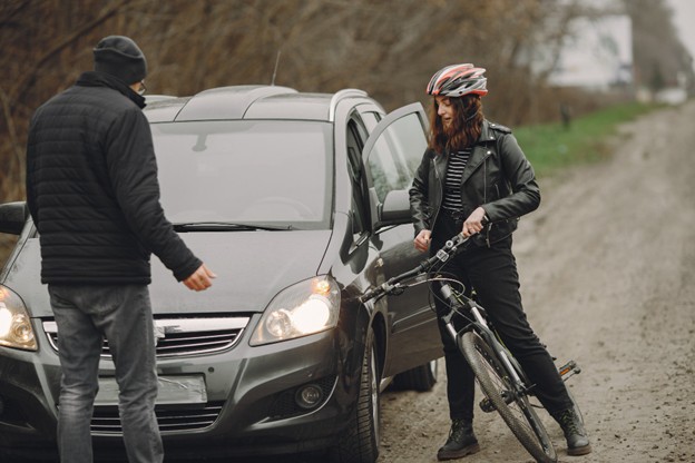 Cyclist wearing helmet stands next to car on roadside while speaking with driver
