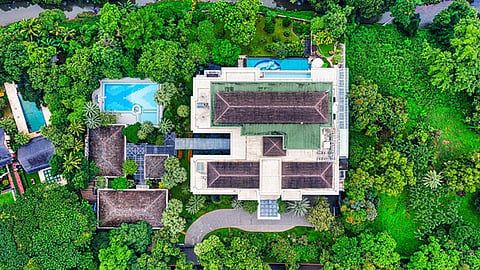 Aerial view of large luxury home surrounded by dense green trees with pool and garden