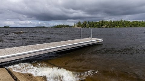 A lakeside dock extends into choppy water beneath dark storm clouds and a distant treeline
