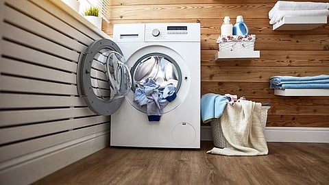 Front-loading washing machine in a modern laundry room with shelves and towels