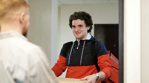 Food delivery courier handing a boxed meal to a customer at home doorway