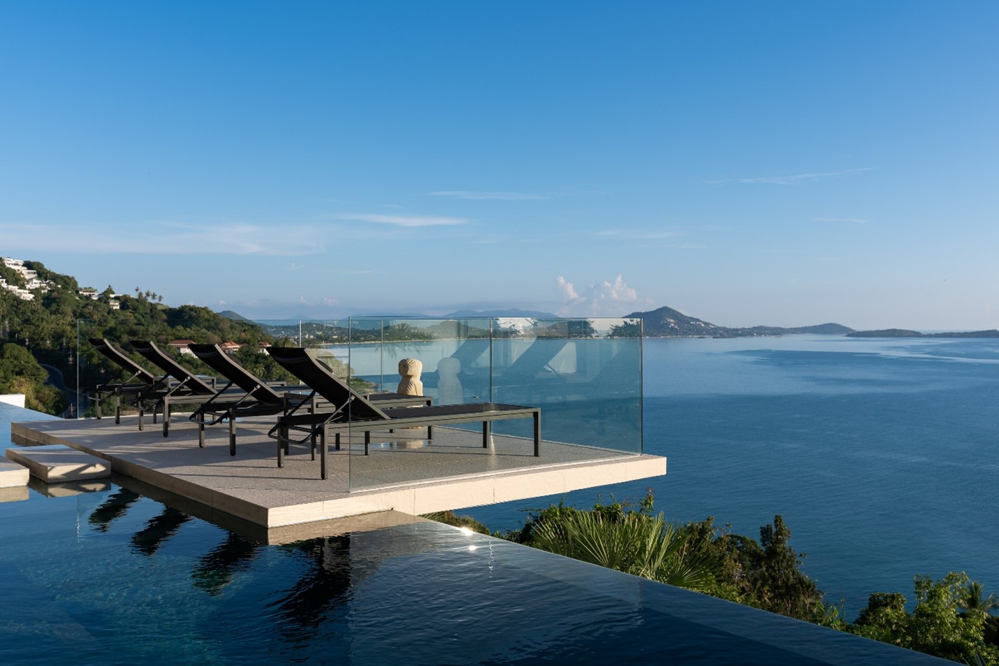 Infinity pool with lounge chairs overlooking ocean and tropical coastline