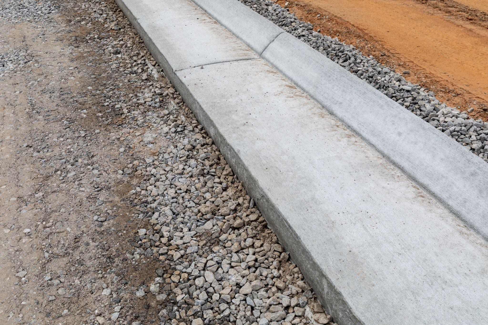 Concrete curb edging installed along gravel and dirt landscaping border