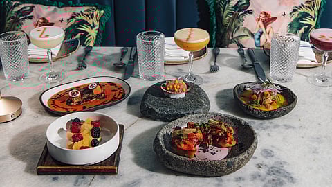 Tasting menu dishes and cocktails arranged on marble table with booth seating