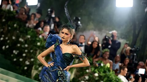 Model posing in dramatic couture gown at a red carpet event with photographers in the background