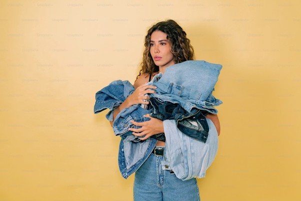 Woman holding a stack of folded denim clothing against a neutral background