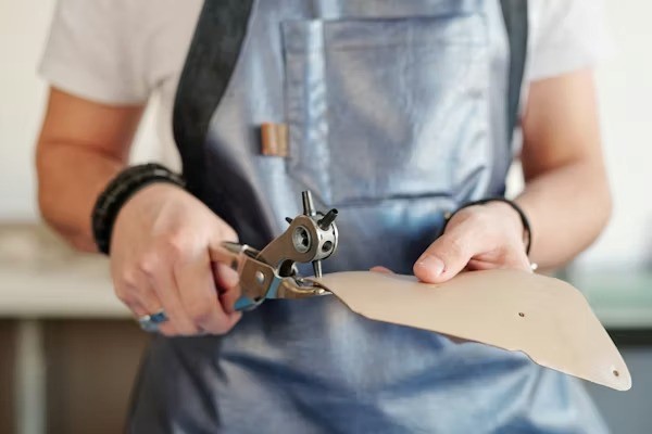 Hands cutting leather with tool in workshop showing craftsmanship process