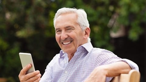 Smiling older man sitting outdoors holding smartphone and enjoying relaxed retirement lifestyle