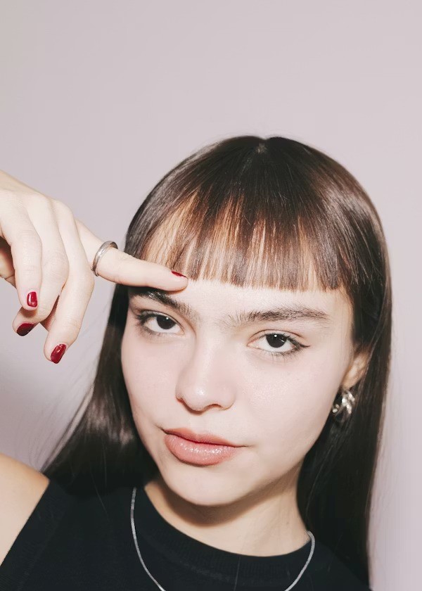 Woman with straight hair and short bangs pointing at fringe to highlight hairstyle choice